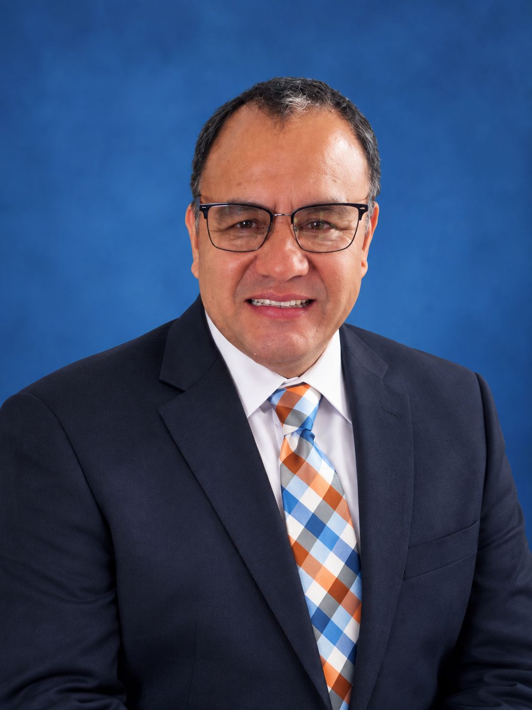 Jorge Carrillo, owner and driver of US1 Driver, smiling in a navy suit and plaid tie.